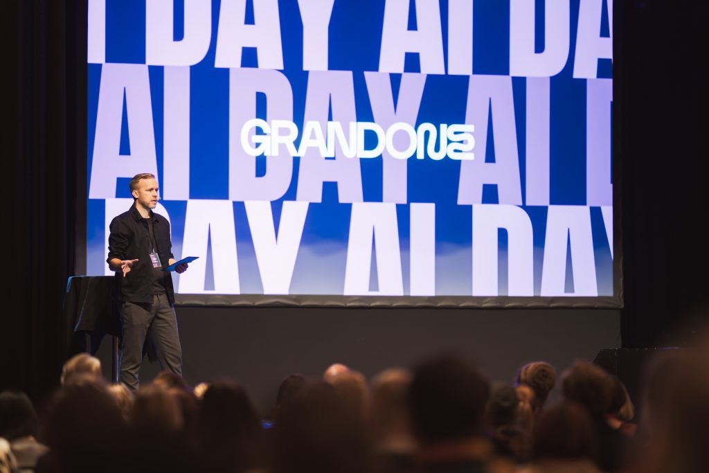 Host speaking to the audience at Grand One AI Day 2025